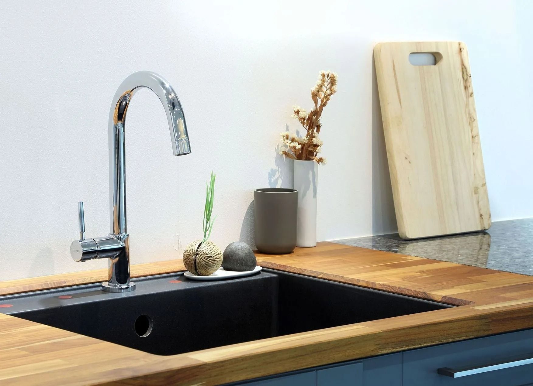 Chrome faucet over black sink in kitchen with wooden countertop; cutting board and decor in background.