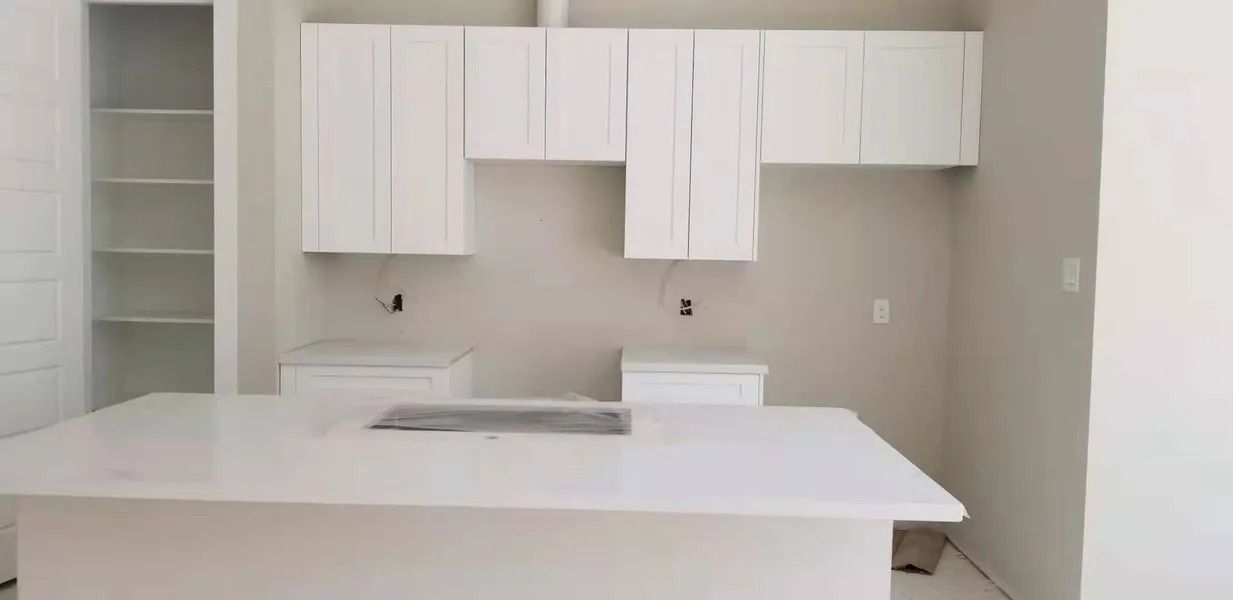 White kitchen with cabinets, island, and shelving. Construction in progress.