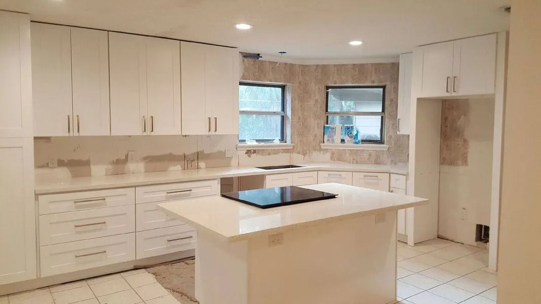 White kitchen with island, cabinets, countertops, and two windows.