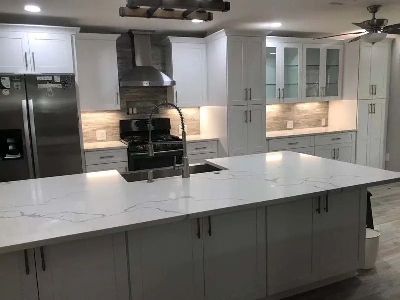 Modern white kitchen with island, stainless steel appliances, and quartz countertops.