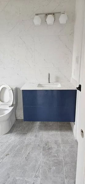 Bathroom with a blue vanity, white countertop, and gray tiled floor. White marble-look wall.