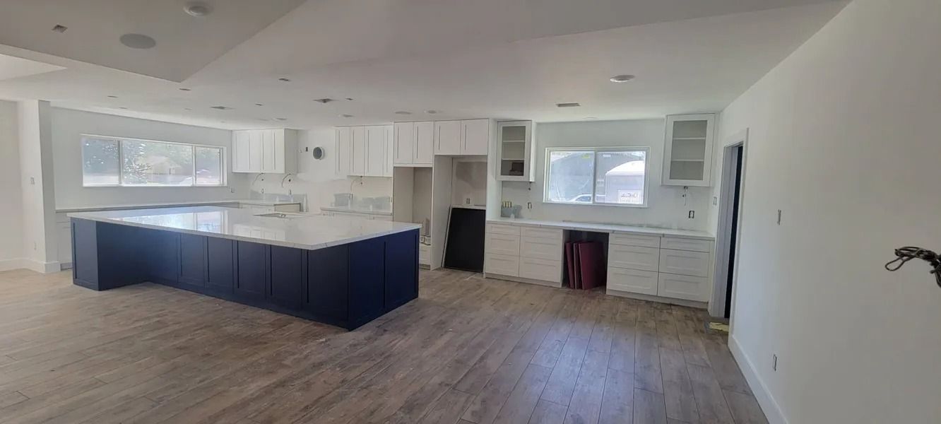 Spacious kitchen with a navy blue island, white cabinets, and wooden floors under construction.