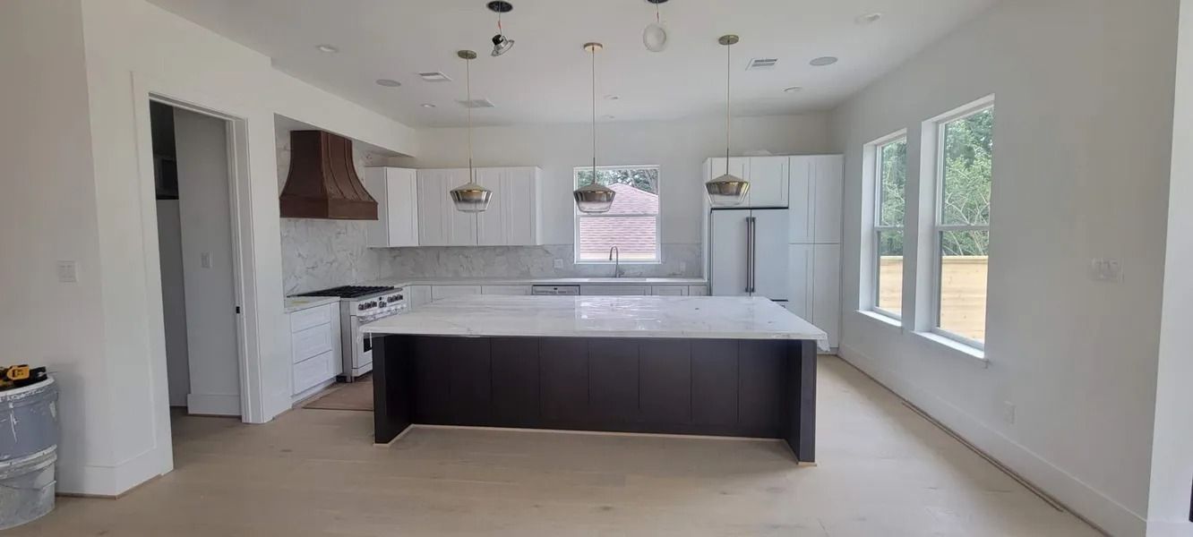 A mostly empty modern kitchen with light wood floors and white cabinets. A dark island sits in the center.