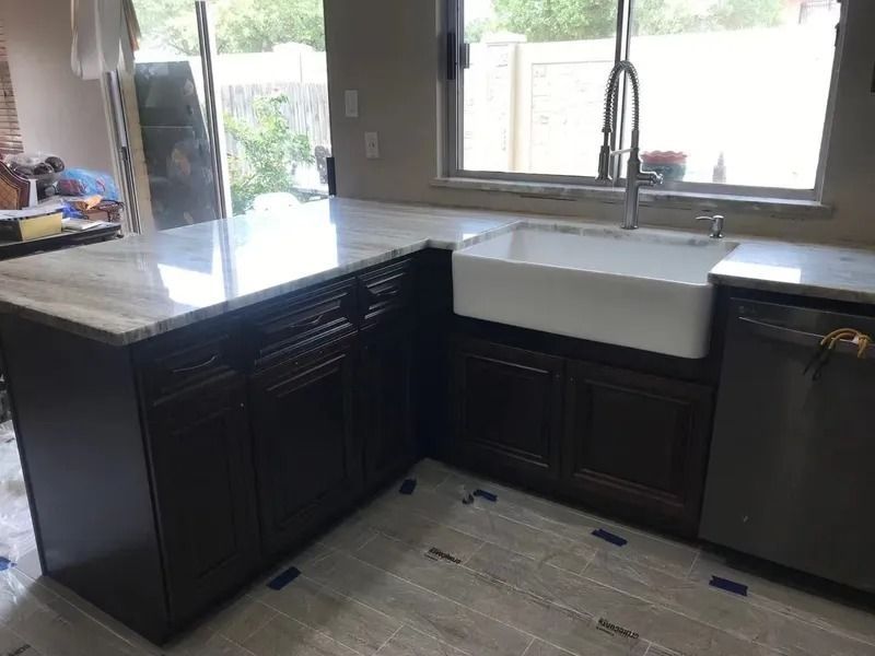 Kitchen island with dark cabinets, light countertop, farmhouse sink, and stainless steel dishwasher.