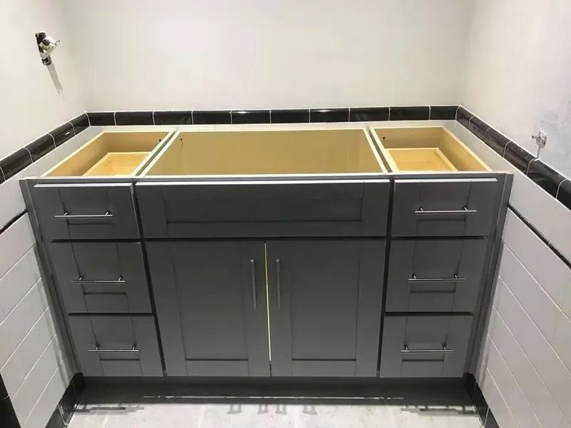 Gray bathroom vanity with drawers and cabinets installed. Unfinished walls surround.