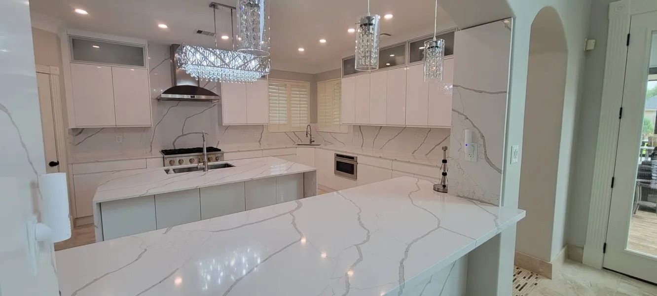 A modern white kitchen with marble countertops, cabinets, and a kitchen island. Bright lighting.