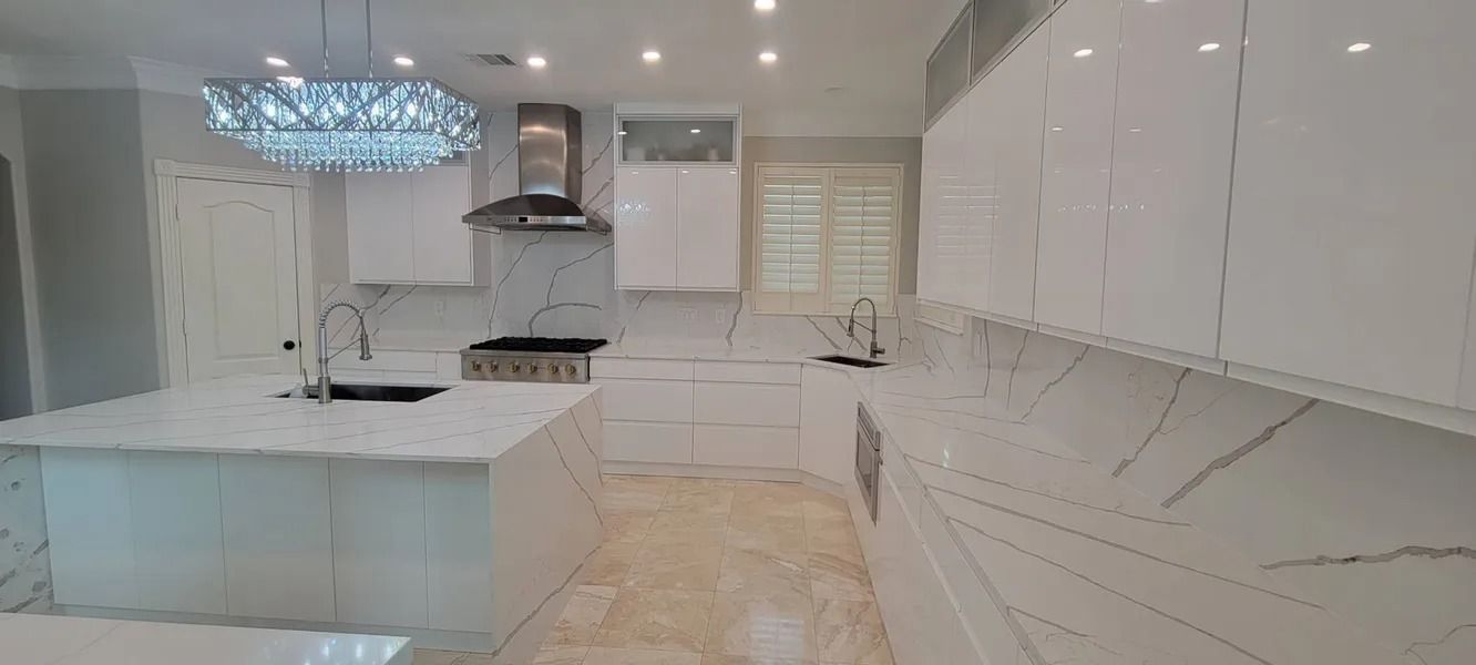 Modern white kitchen with marble countertops, island, and cabinets. A decorative light hangs above.