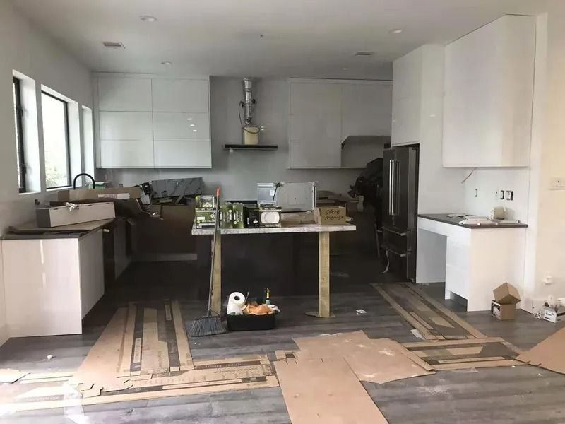 Kitchen under construction, white cabinets, island with wood supports, flooring in progress.
