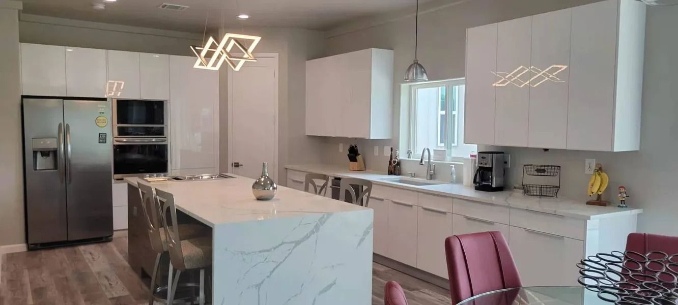 Modern white kitchen with stainless steel appliances, marble island, and decorative light fixtures.