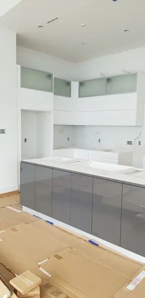 Modern kitchen with gray cabinets, white countertops, and white backsplash in a room with hardwood floors.