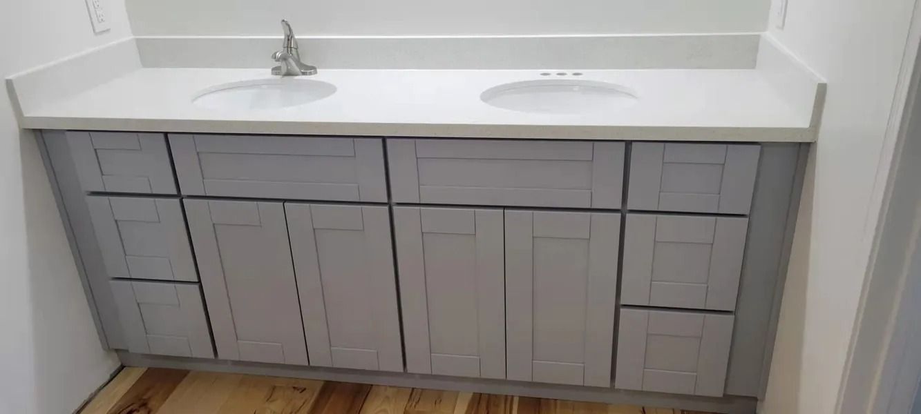 Bathroom vanity with two sinks and gray cabinets. White countertop. Wooden floor.