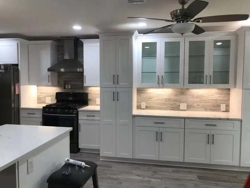White kitchen cabinets, black appliances, a central island, and wood-look flooring.