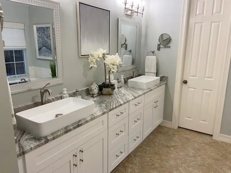Bathroom with double vanity, white cabinets, rectangular sinks, marble countertop, and decorative orchids.