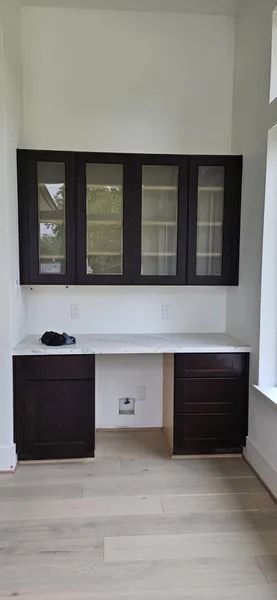 Built-in dark brown desk with upper cabinets and a white countertop. Light wood flooring.