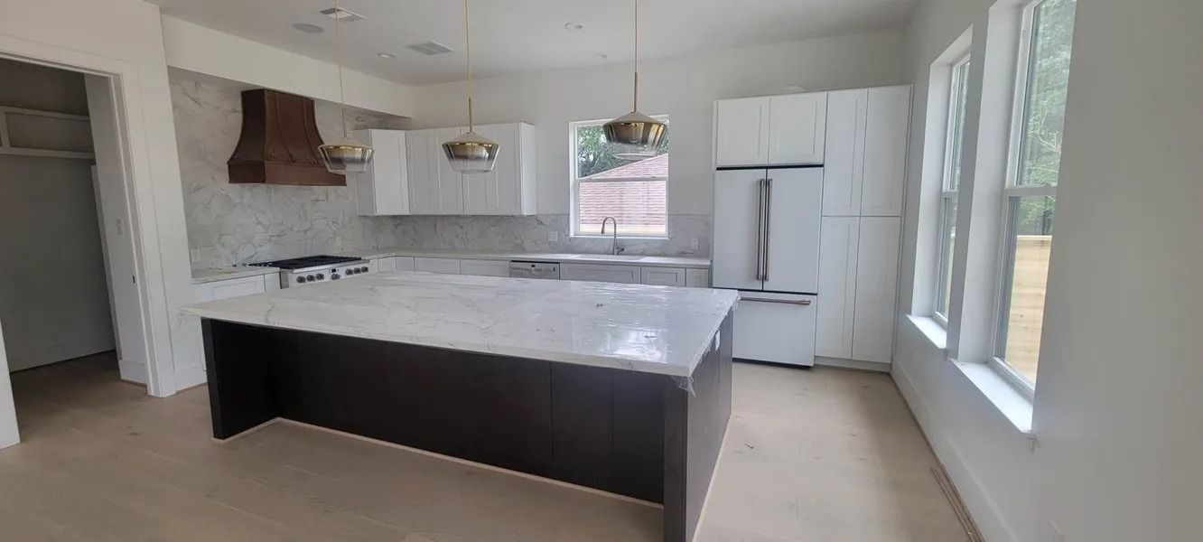 Kitchen with a large island, white cabinets, stainless steel refrigerator, and windows.