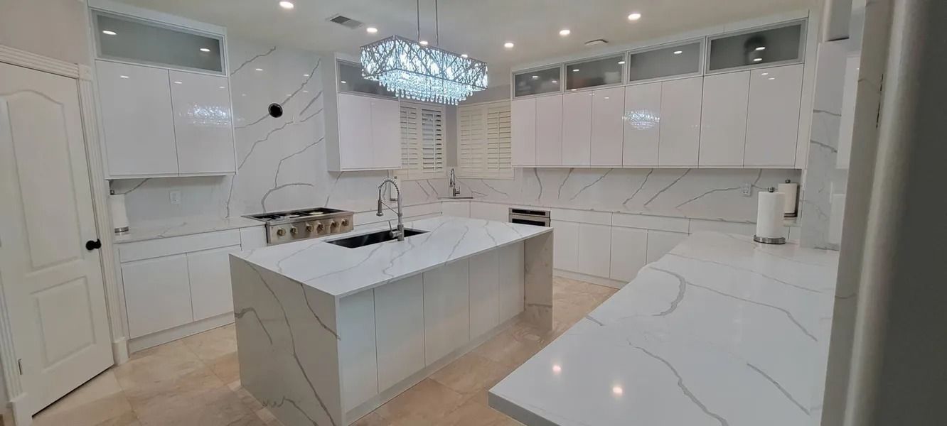 Modern white kitchen with marble countertops, cabinets, and a chandelier.