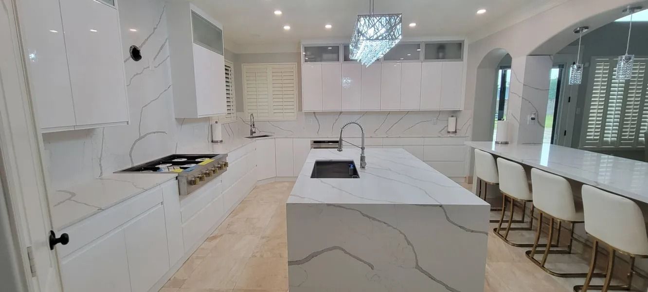 Modern all-white kitchen with marble countertops, central island, and a dining bar with stools.