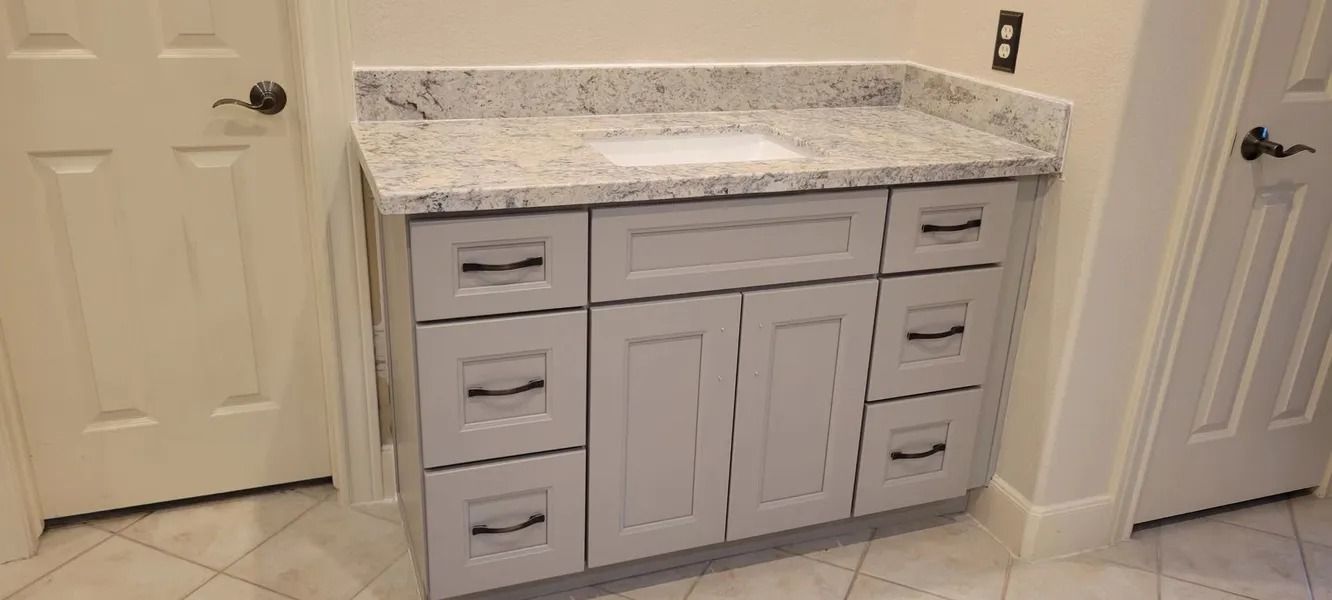 Gray bathroom vanity with drawers and cabinets, granite countertop, between two white doors.