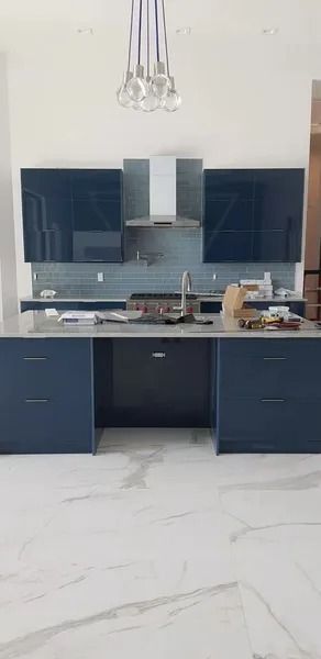 Modern kitchen with navy blue cabinets, stainless steel range hood, and white marble floor.