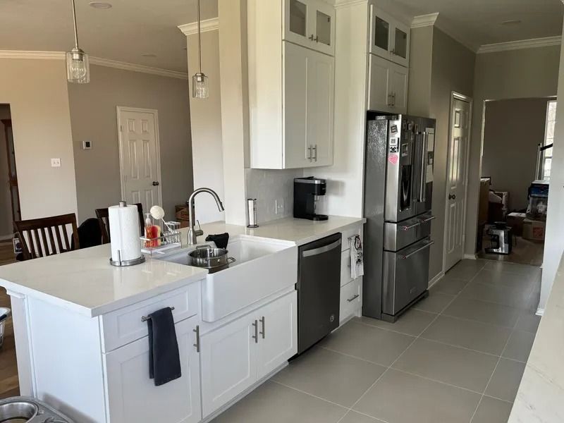 White kitchen with island, cabinets, stainless steel refrigerator and sink.