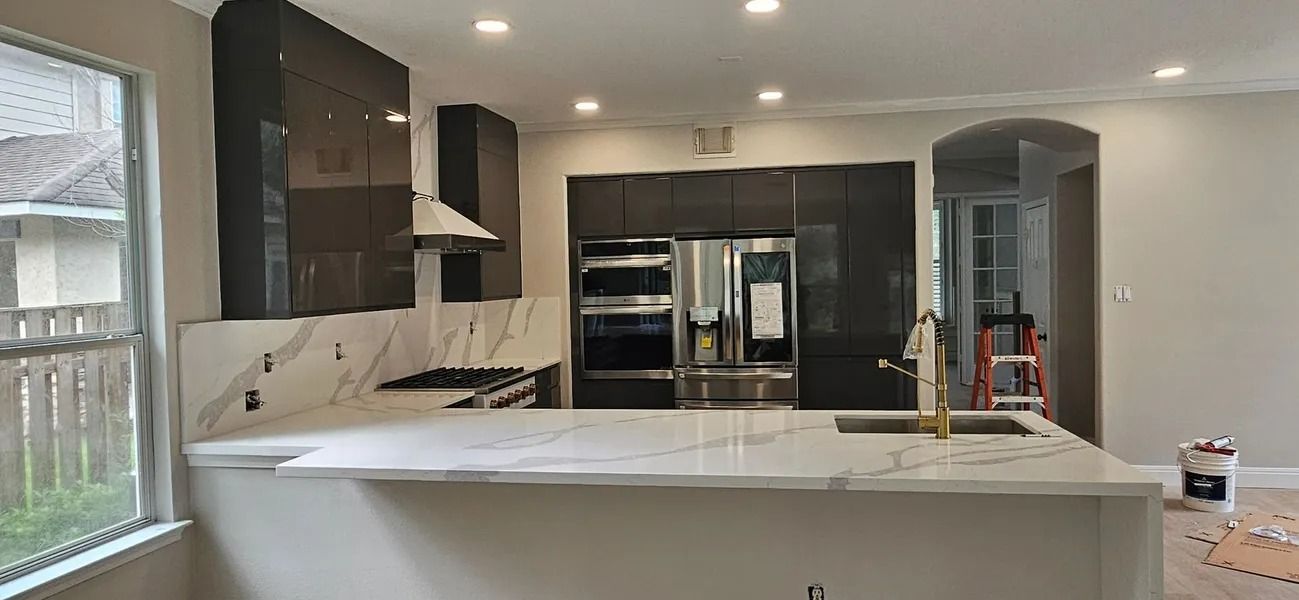 Modern kitchen with dark cabinetry, white countertops, stainless steel appliances, and gold faucet.