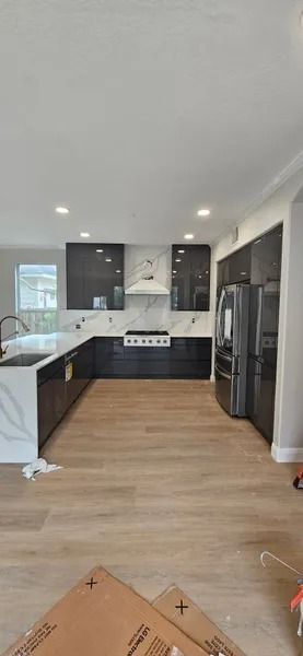 Modern kitchen with black cabinets, marble backsplash and island, and light wood floors.