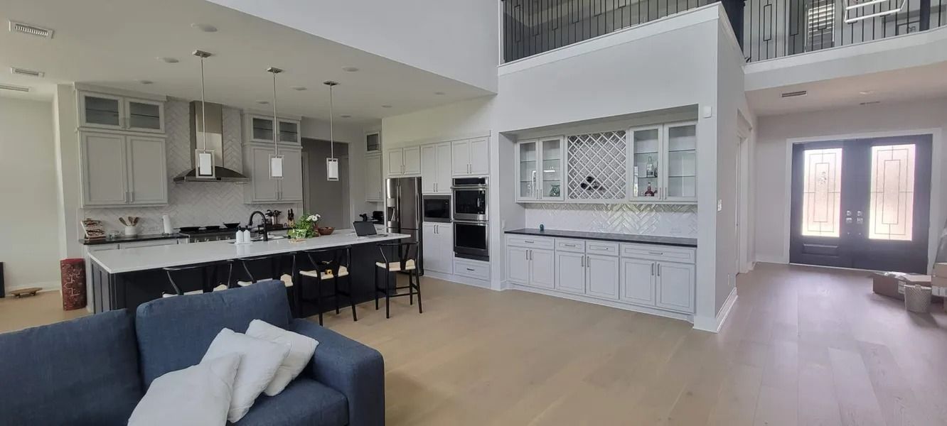 Open-concept kitchen and living area, white cabinets, black island, blue sofa, and tall entryway doors.