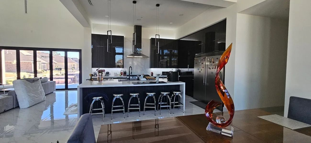 Modern kitchen with dark cabinetry, large island with seating, open to living area with folding glass doors.