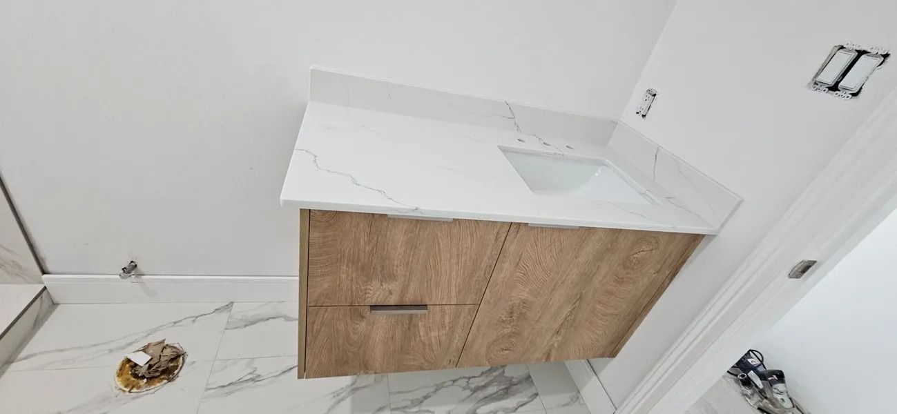 Bathroom vanity with light wood cabinet, white countertop, and white tile floor. Wall is white.