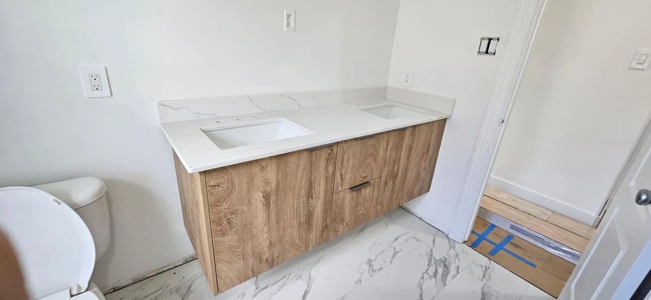 Bathroom with a floating wood vanity with a marble countertop, white walls, and a toilet.