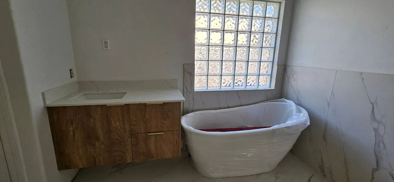 Bathroom with a white bathtub and wood-toned vanity under a window with glass blocks.
