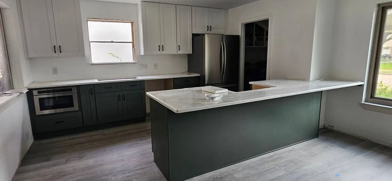Modern kitchen with white and dark green cabinets, stainless steel appliances, and a marble island.