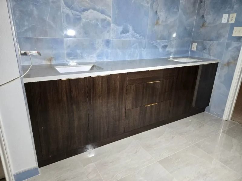 Dark wood vanity with dual sinks, gray countertop, blue marbled tile backsplash, and light gray tiled floor.
