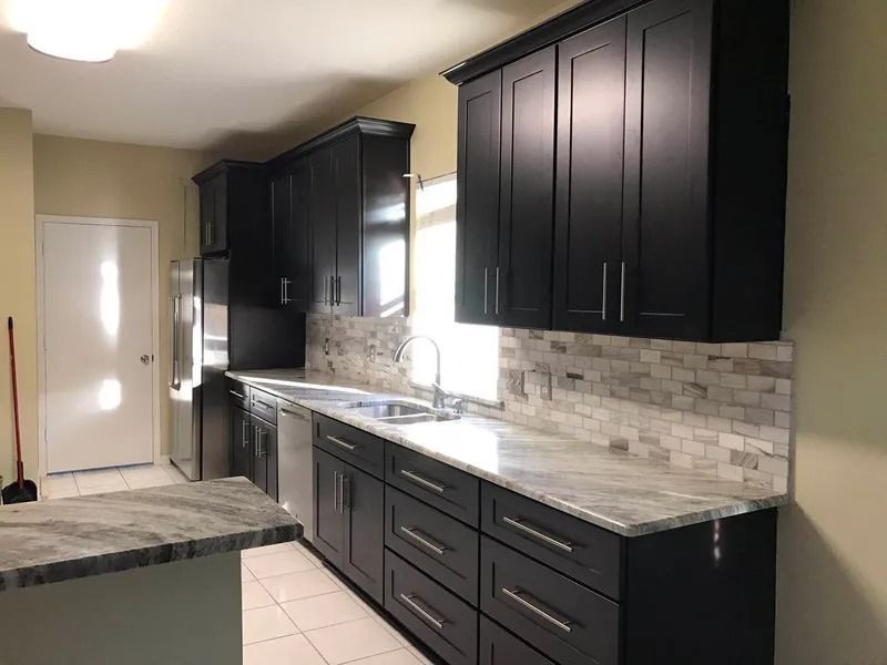 Black kitchen cabinets with granite countertops and tiled backsplash.