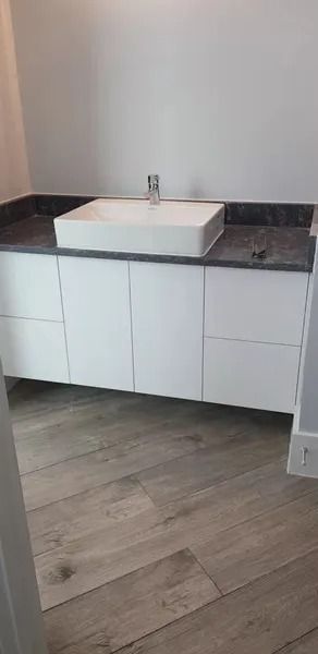 White bathroom vanity with rectangular sink and dark countertop, wooden-look flooring.