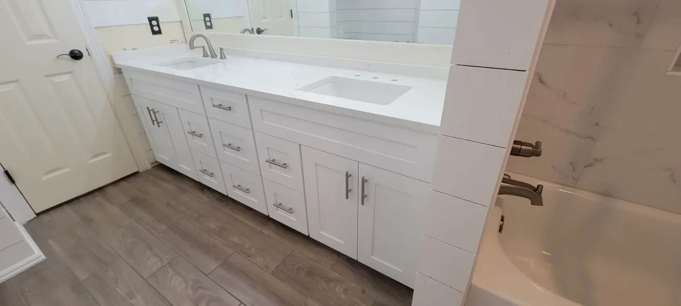 Bathroom with white cabinets, countertop, and bathtub. Light gray flooring. Mirror above sink.