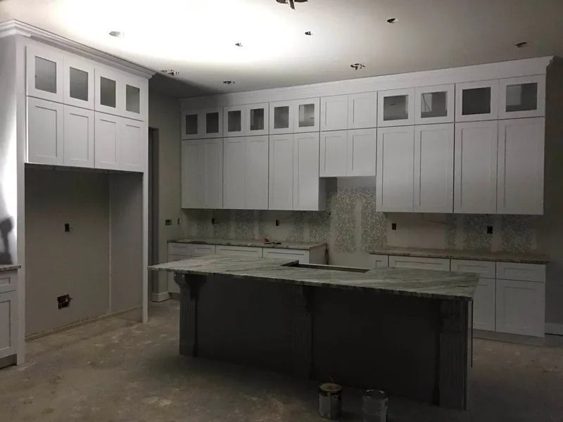 White kitchen cabinets under construction; an island with granite countertop.