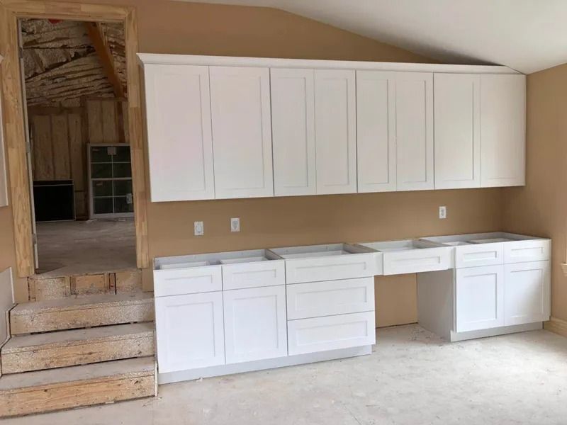 White kitchen cabinets installed against a tan wall, with a doorway visible to the left.