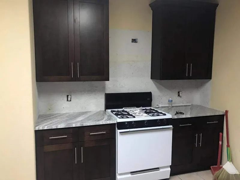 Kitchen with dark cabinets, white appliances, and marble countertops. Partially tiled backsplash is present.