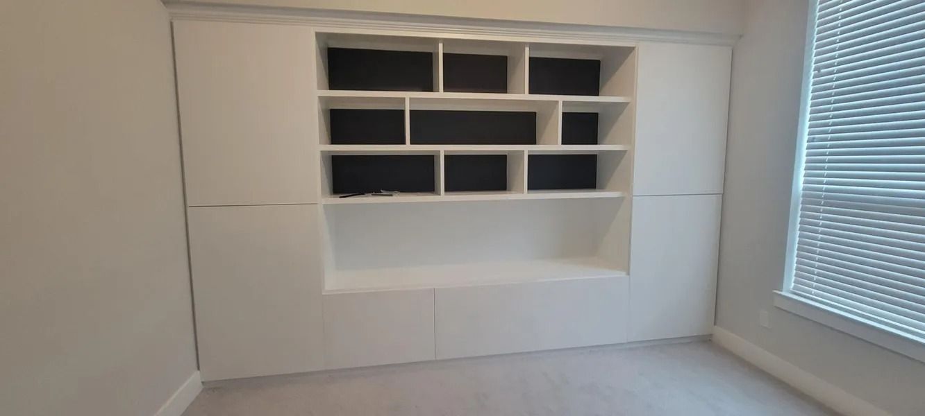 White built-in shelving unit with a variety of cubby sizes, against a white wall in a room, with a window.