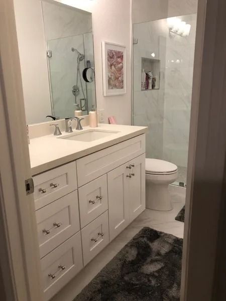 Bathroom with white vanity, sink, and shower, light gray flooring, and a decorative rug.