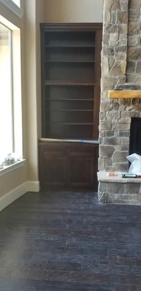 Built-in dark wood bookshelf next to a stone fireplace in a room with dark wood flooring.