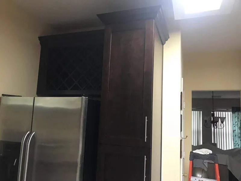 Dark wooden cabinets above a stainless steel refrigerator. Kitchen setting, a wine rack visible.