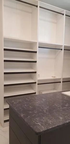 White built-in closet with shelves, hanging rods, and a dark countertop on an island.
