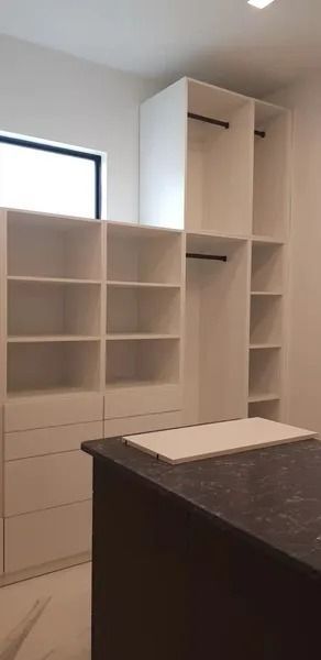 A walk-in closet with white shelving and drawers. A dark counter is in the foreground.