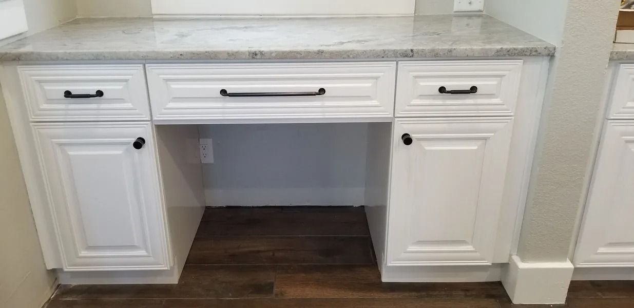 White built-in desk with granite countertop and black hardware. Dark wood floor.