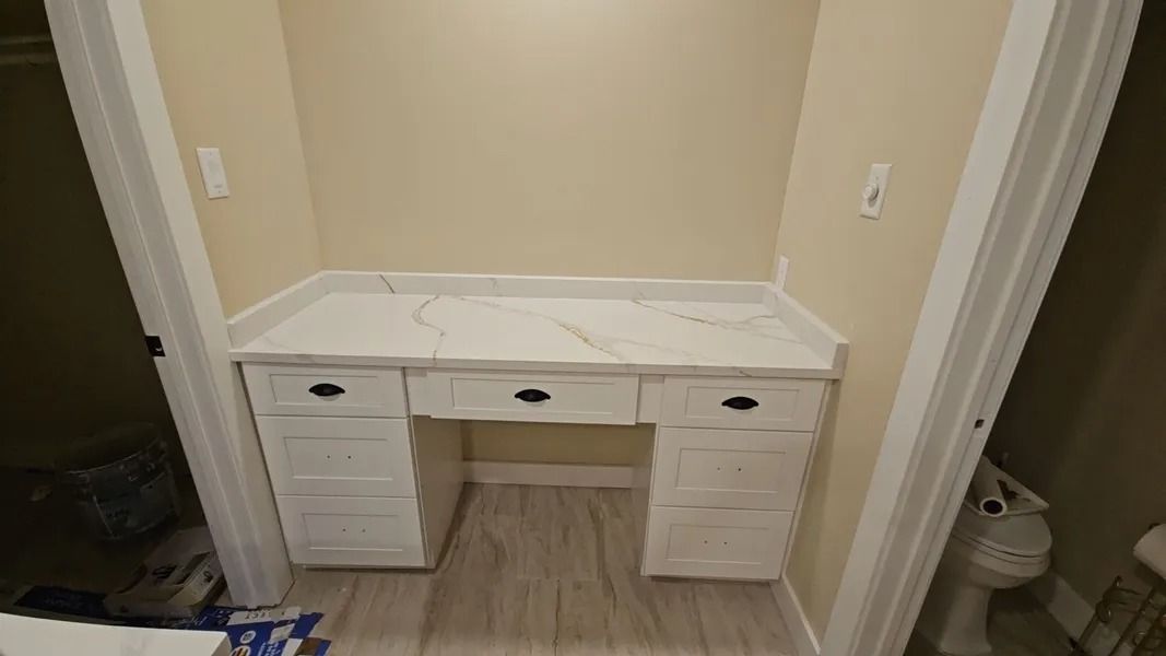 Built-in white desk with marble countertop, three drawers, and two side cabinets in a neutral alcove.
