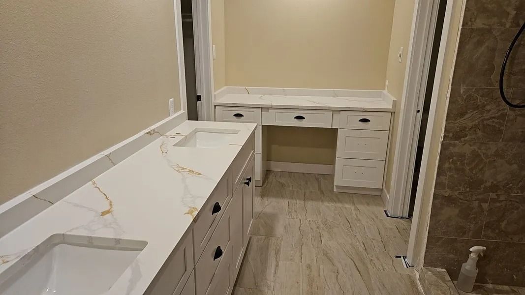 Bathroom with white and gold countertop, white cabinets, and beige walls.