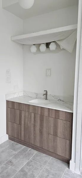Bathroom with wooden vanity, marble countertop, and three-bulb light fixture.