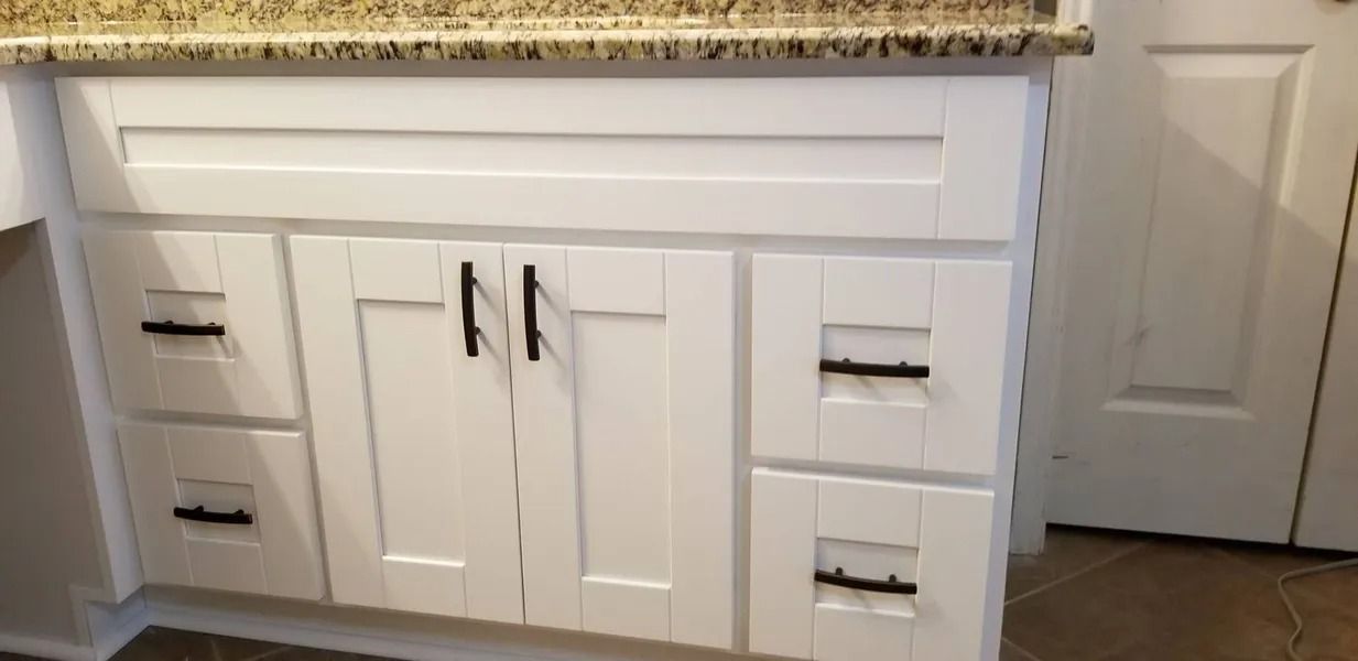 White bathroom vanity with black hardware and a granite countertop. A white door is visible in the background.
